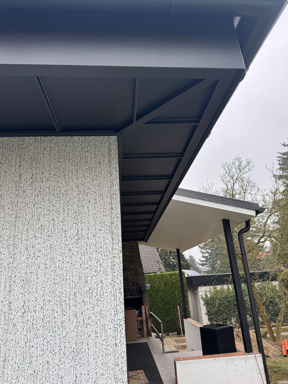 Sicht auf den modernen Dachüberstand eines Hauses mit grauem Dach und strukturiertem Wandsystem.