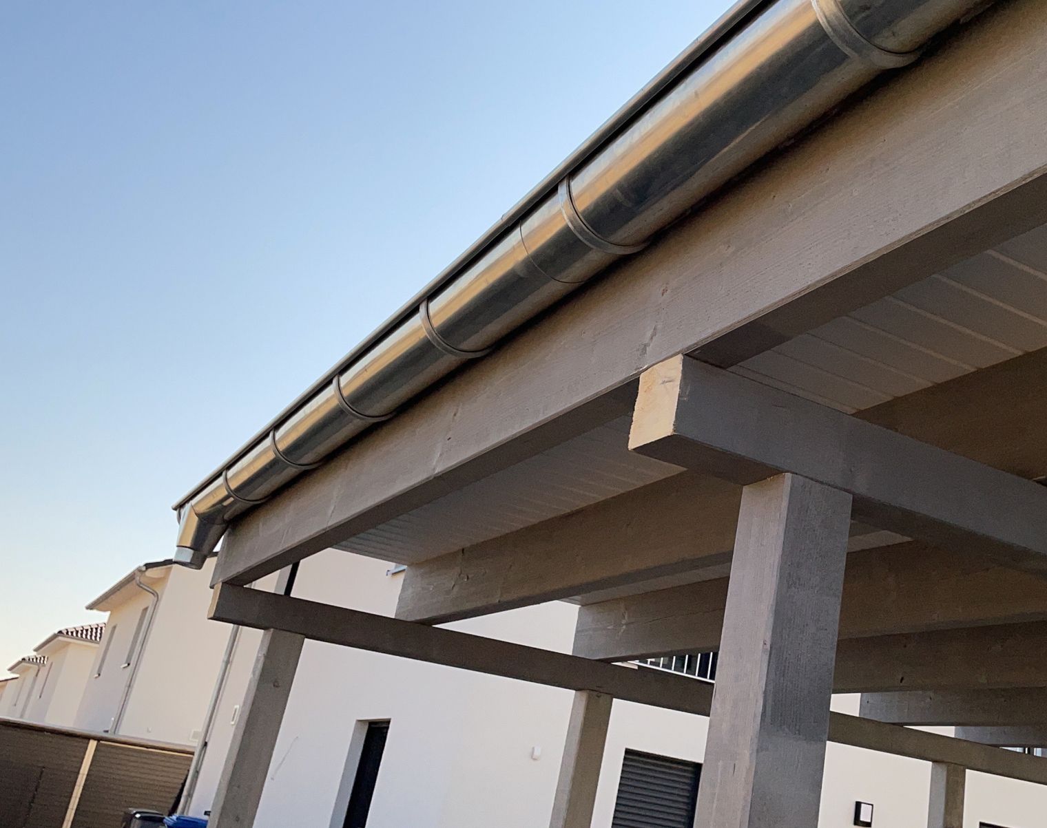 Sicht auf einen Dachüberstand mit einer silbernen Dachrinne und Holzstützen.