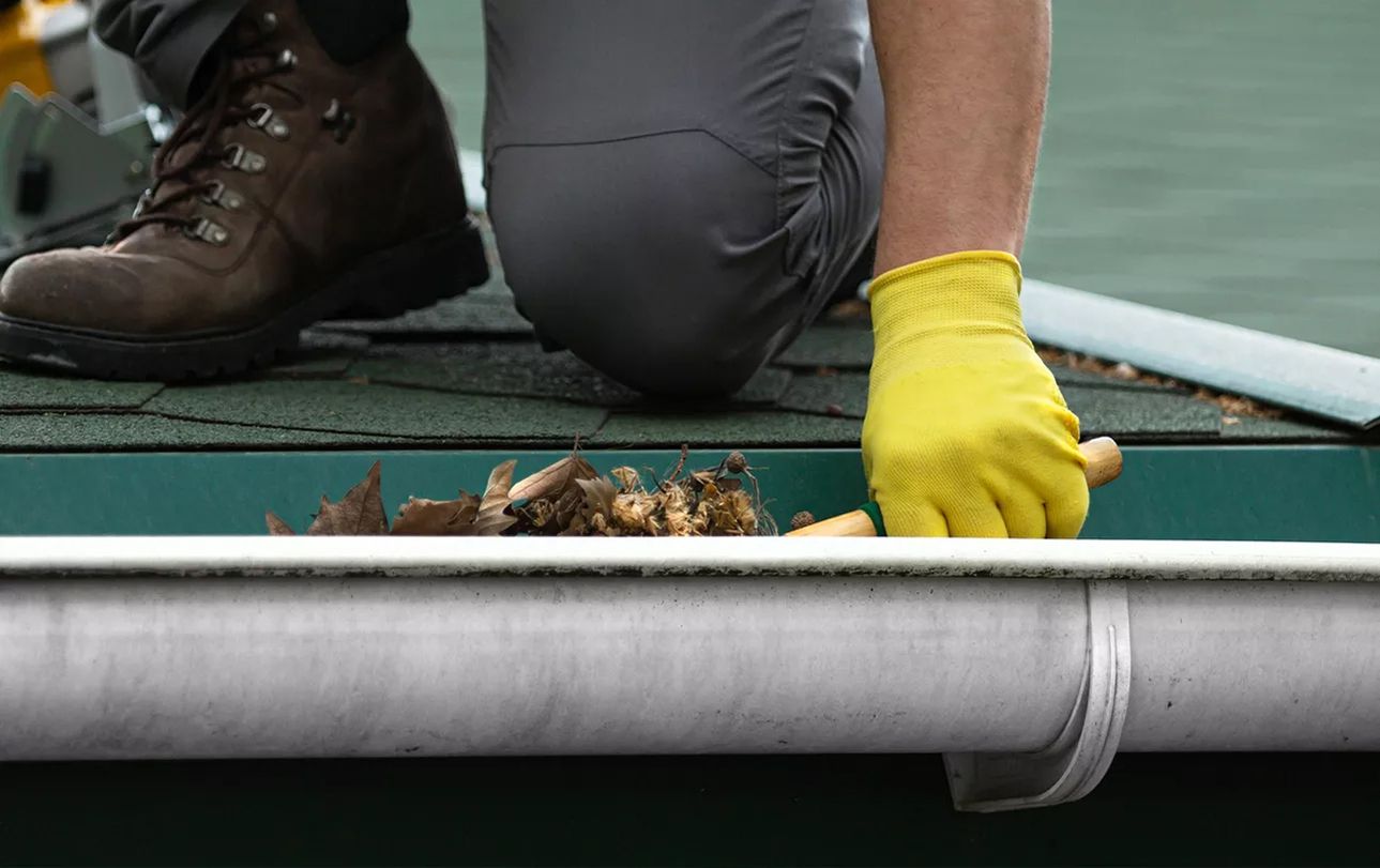 Person reinigt die Dachrinne mit Handschuhen und einem Werkzeug
