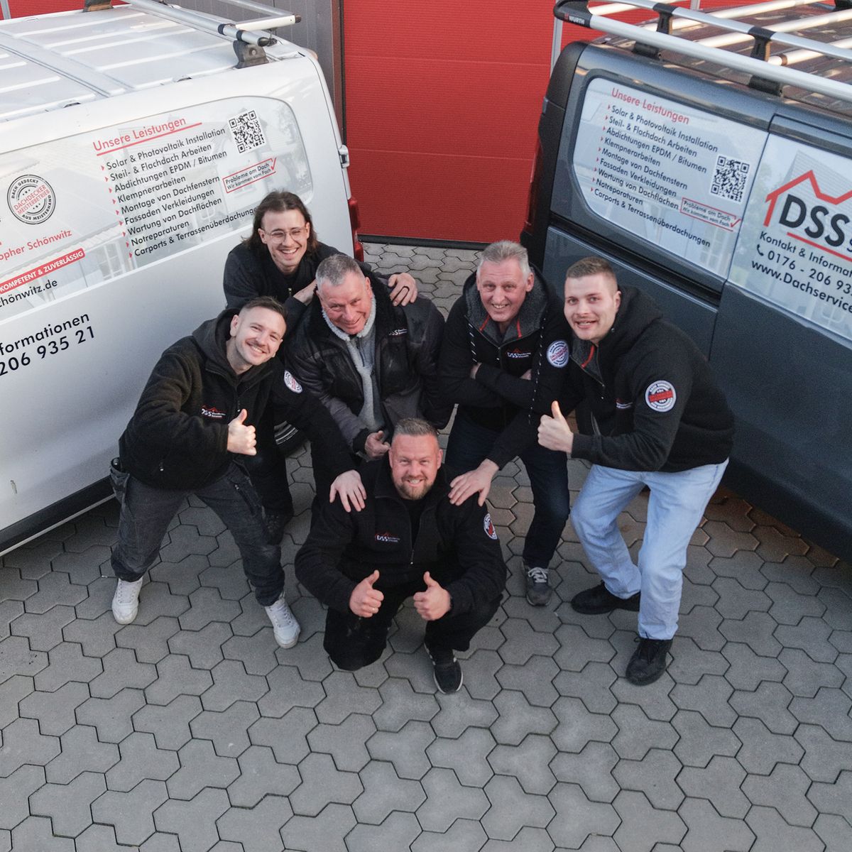 Das Team der Dachdeckerfirma posiert vor ihren Fahrzeugen.